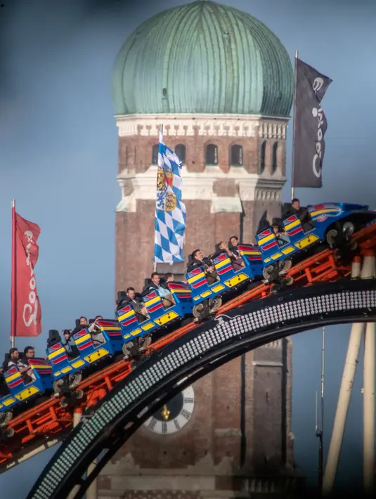 Pengunjung menaiki roller coaster di dekat Katedral Bunda Maria selama festival bir Oktoberfest di Munich, 24 September 2018. Oktoberfest adalah rangkaian festival terbesar di dunia yang diadakan setiap tahun di Jerman. (AFP/dpa/Peter Kneffel/Germany OUT)