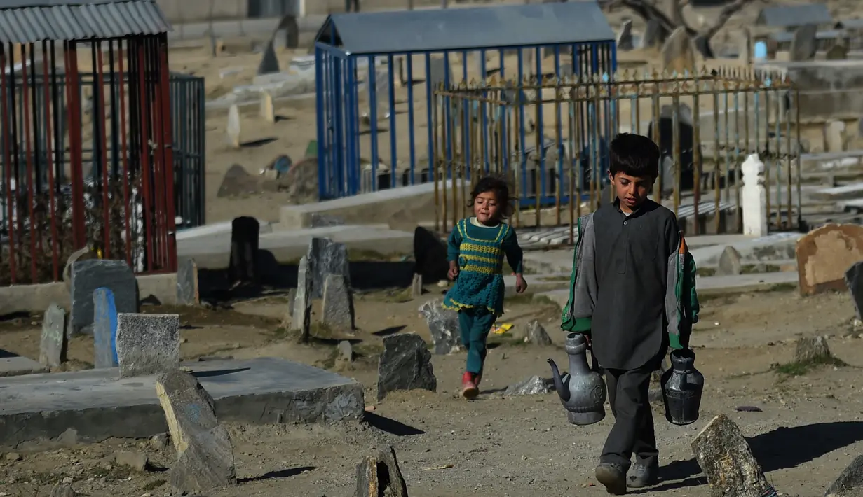 Afghan Zilgai (9) berjalan bersama adiknya, Khushnuma (4), ketika mencari pelanggan di pemakaman Kart-e-Sakhi, Kabul, 20 Februari 2016. Afghan setiap hari menjual air kepada para peziarah dengan penghasilan 1,5 USD/hari. (AFP PHOTO/Wakil KOHSAR)