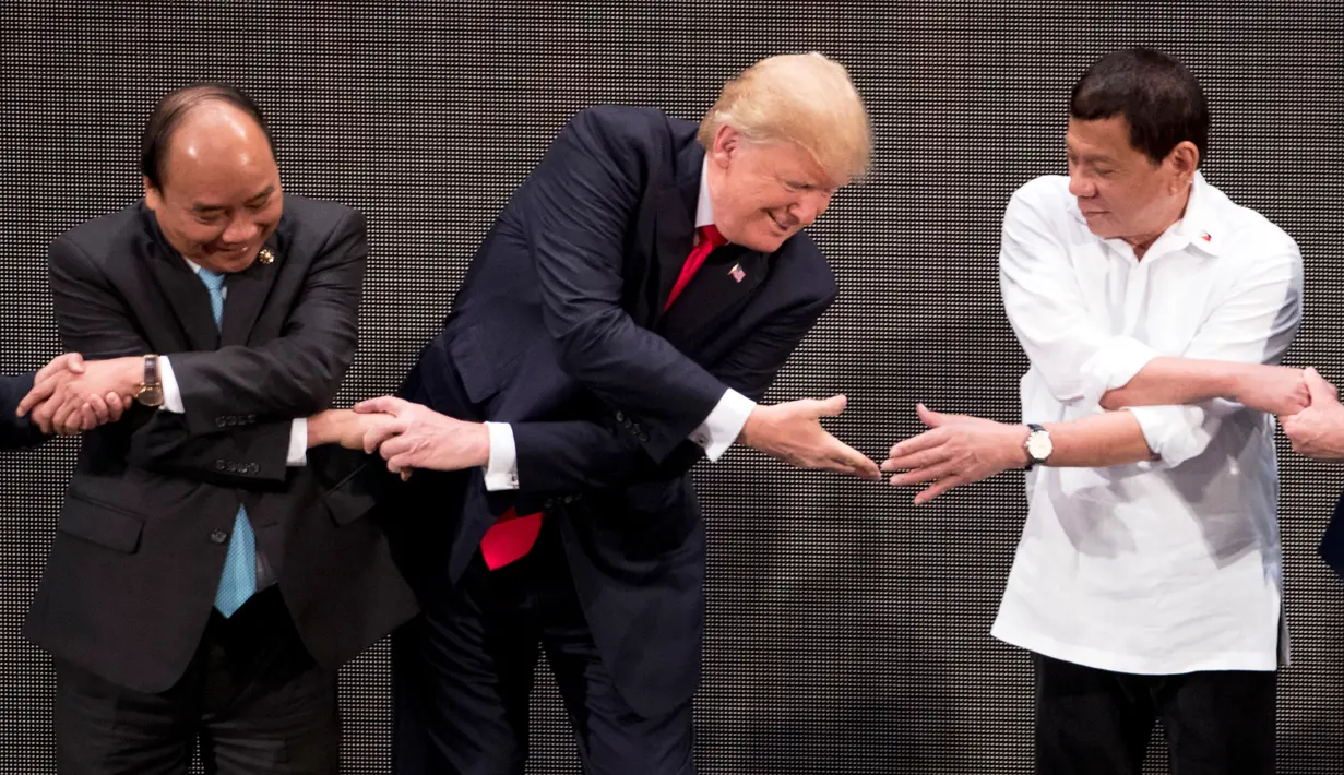 Tangan kanan Presiden AS, Donald Trump berusaha menjabat tangan Presiden Filipina, Rodrigo Duterte saat salaman khas ASEAN di upacara pembukaan KTT ASEAN, Manila, Senin (13/11). Trump tampak sulit mengikuti gaya salaman pemimpin lainnya (AP/Andrew Harnik)