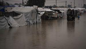 Warga Palestina menyeberangi jalan yang tergenang banjir setelah hujan lebat di Khan Younis, Jalur Gaza selatan, Kamis 11 Desember 2025. Hujan deras di Khan Younis menyebabkan kondisi kemanusiaan di kamp-kamp pengungsi menjadi sangat kritis. (AP Photo/Abdel Kareem Hana)