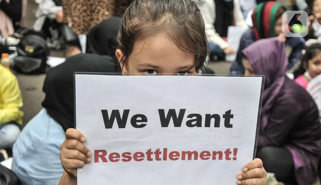 Seorang anak pencari suaka membawa poster saat ikut aksi di depan Kantor UNHCR, Jakarta, Senin (15/11/2021). Ratusan pencari suaka asal Afghanistan menuntut segera dipindahkan ke negara ketiga yang terbebas dari perang setelah lebih 10 tahun mengungsi di Indonesia. (merdeka.com/Iqbal S Nugroho)