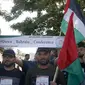 Warga Palestina di Kota Gaza pada 24 Juni 2019, mengibarkan bendera nasional dan memegang spanduk yang mengecam konferensi Perdamaian untuk Kemakmuran yang dipimpin AS di Bahrain. (MOHAMMED ABED / AFP)