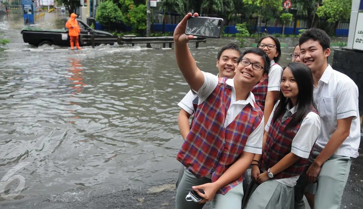 Sejumlah pelajar berselfie  di dekat genangan air di depan kampus UKRIDA, Jakarta, Selasa (21/1). Hujan deras sejak malam tadi, membuat sejumlah wilayah Jakarta tergenang air banjir. (Liputan6.com/Gempur M Surya)
