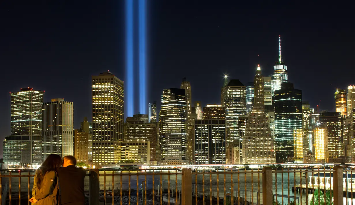 Sepasang kekasih menikmati ‘Tribute in Light’ dari sisi Brooklyn Promenade untuk mengenang tragedi serangan WTC di New York, Minggu (10/9). Kota New York memperingati 16 tahun tragedi serangan bom pada 11 September 2001 silam. (AP Photo/Mark Lennihan)