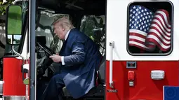 Presiden AS, Donald Trump duduk sambil memeriksa sebuah truk pemadam kebakaran saat bersama Wapres Mike Pence menghadiri acara pameran produk bertajuk "Made in America" di Gedung Putih, Washington, Senin (17/7). (Olivier Douliery/AFP)