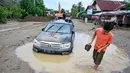 Sejumlah kendaraan roda dua dan roda empat milik warga juga ikut hanyut terbawa air sungai. Tampak dalam foto, warga berjalan melewati mobil yang terdampar di lumpur tebal akibat banjir bandang di Meureudu, Kabupaten Pidie Jaya, Provinsi Aceh, Jumat 28 November 2025. (CHAIDEER MAHYUDDIN/AFP)