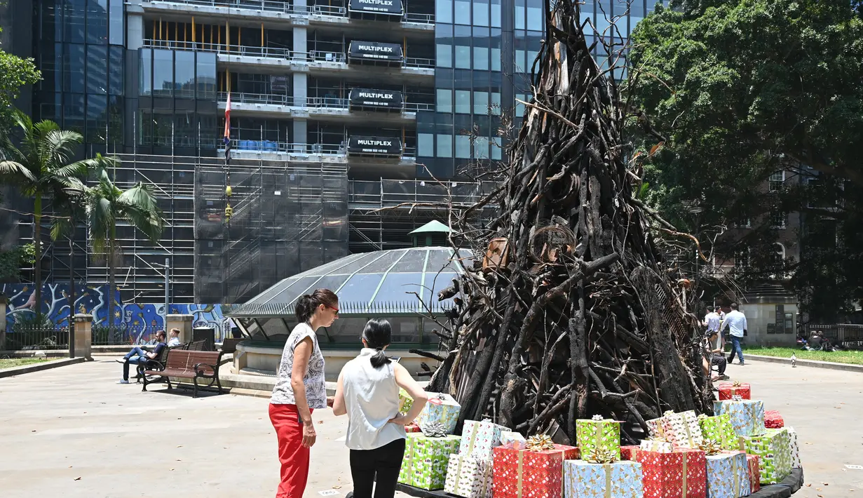Dua wanita melihat instalasi yang dijuluki 'Pohon Natal yang Terbakar' di Sydney (18/12/2019). Warga Australia di pantai timur bersiap menghadapi "ancaman baru" ketika gelombang panas disertai dengan angin yang bergolak menurunkan lebih dari 100 kebakaran hutan di kawasan itu. (AFP/Peter Parks)