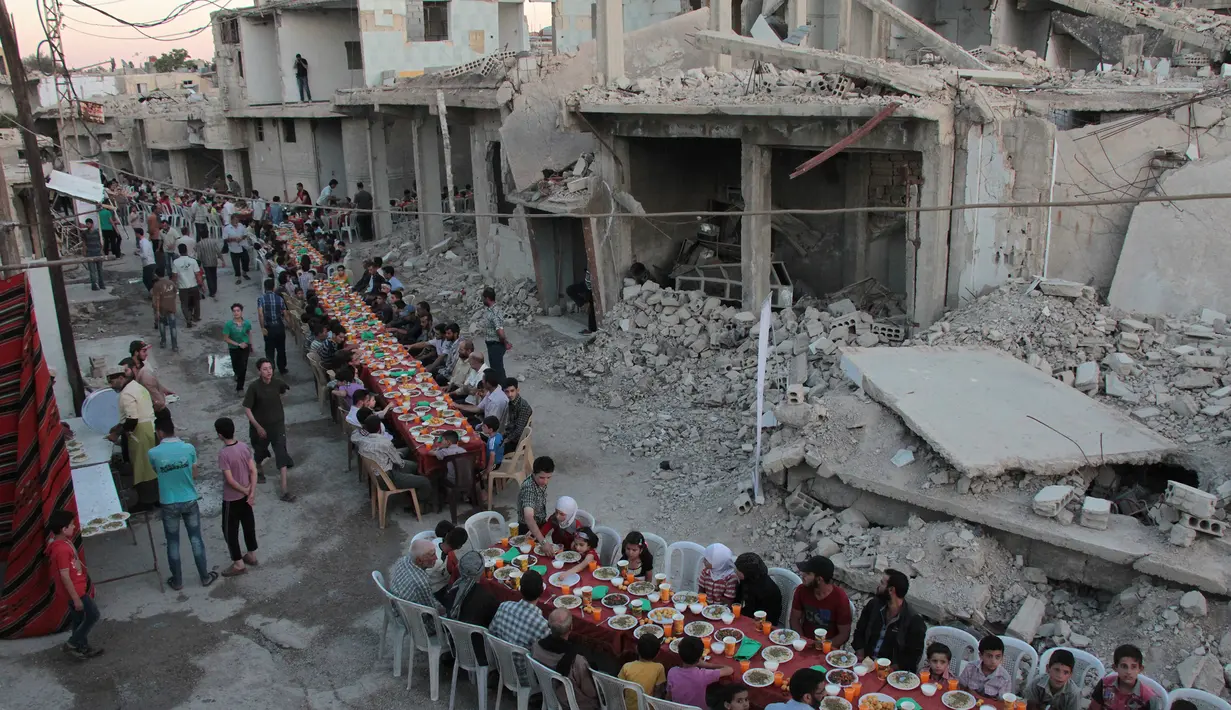 Sejumlah warga bersiap untuk berbuka puasa bersama di tengah reruntuhan bangunan di Kota Douma, yang dikuasai pemberontak di pinggiran ibukota Damaskus, Suriah, (18/6). (AFP Photo/Hamza Al-Ajweh)