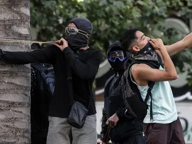 Demonstran berselfie ketika yang lain menggunakan ketapel menyerang polisi selama bentrok memprotes kebijakan ekonomi pemerintah di Santiago (6/11/2019). Presiden Chile mengatakan "tidak menyembunyikan apa-apa" mengenai tuduhan bahwa polisi membunuh, menyiksa warga sipil. (AFP Photo/Javier Torres)
