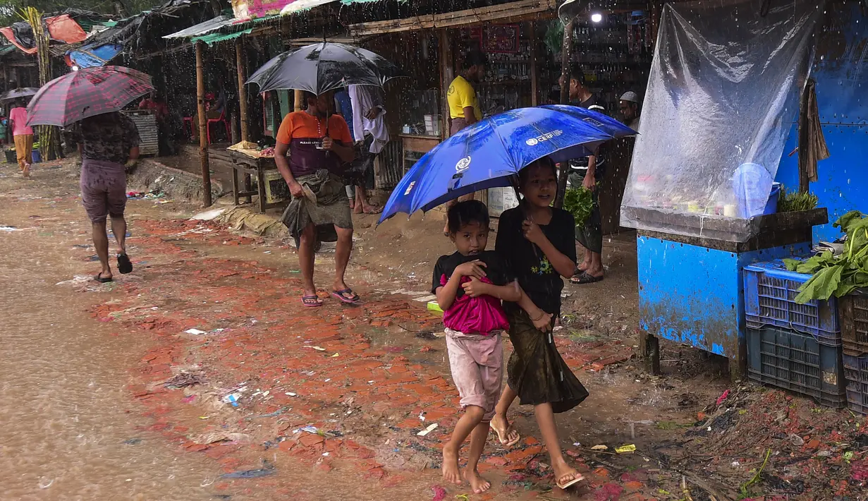 Dua anak pengungsi Rohingya berjalan menggunakan payung saat hujan di kamp pengungsi Kutupalong, Ukhia (12/9/2019). Kamp ini didirikan secara tidak resmi pada tahun 1991, setelah ribuan orang Rohingya melarikan diri dari Operasi Pyi Thaya yang dilancarkan militer Burma. (AFP Photo/Munir Uz Zaman)