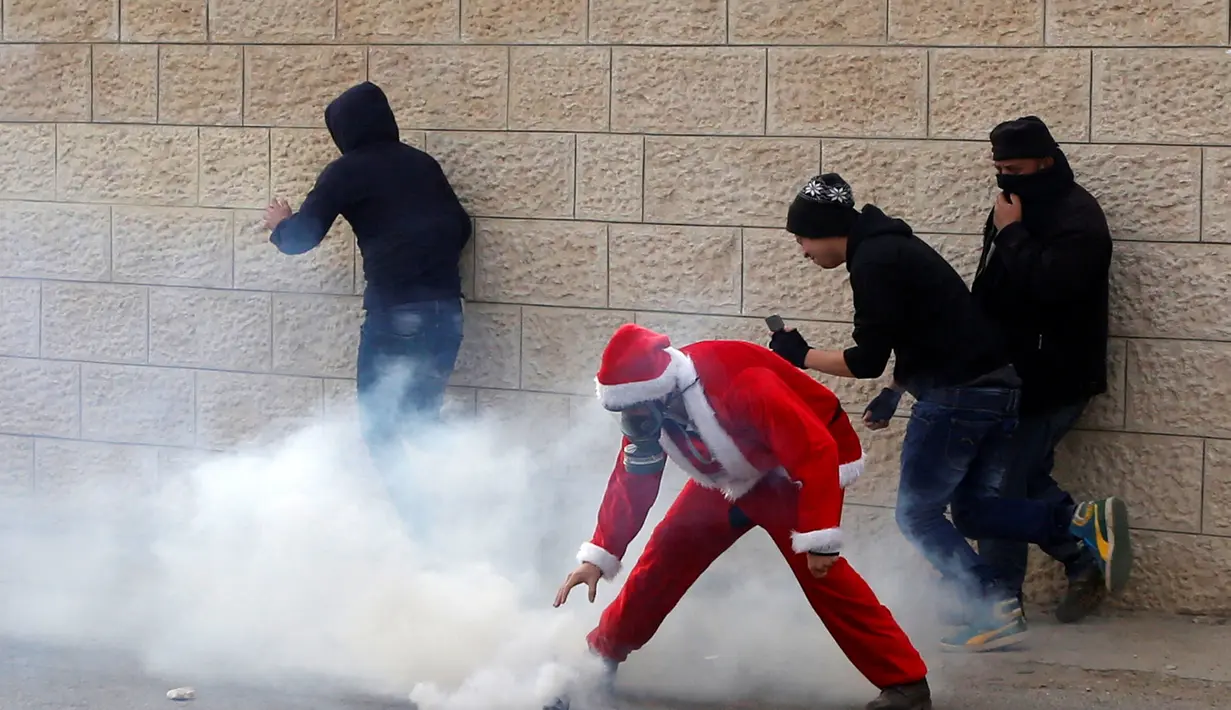 Seorang pengunjuk rasa berkostum Santa Claus berusaha mengambil gas air mata saat aksi di desa Tepi Barat Bilin dekat Ramallah, Jumat (23/12). Mereka menentang pembangunan tembok pembatas di Israel. (REUTERS/Mussa Issa Qawasma)