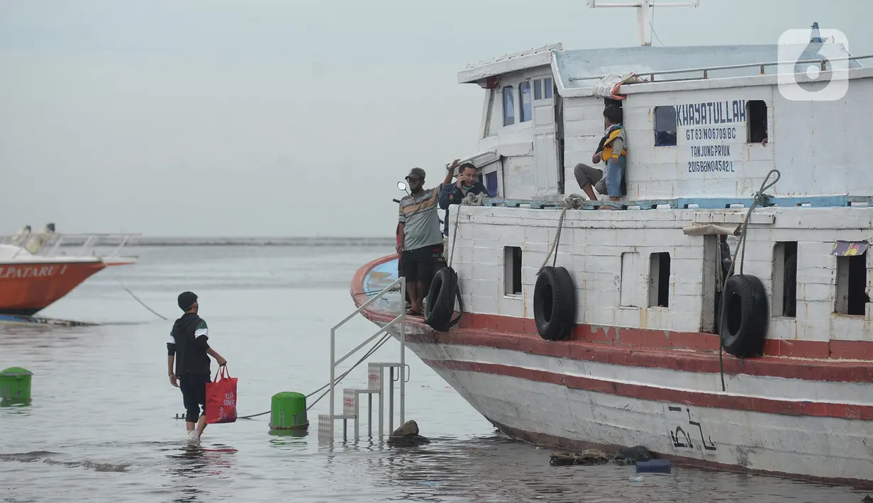Seorang pria melintasi banjir rob di dermaga pelabuhan kali Adem, Muara Angke, Jakarta, Kamis (31/12/2020). Badan Meteorologi Klimatologi dan Geofisika (BMKG) memberikan peringatan dini cuaca akan berpotensi hujan disertai angin kencang dan kilat/petir di pergantian tahun. (merdeka.com/Imam Buhori)