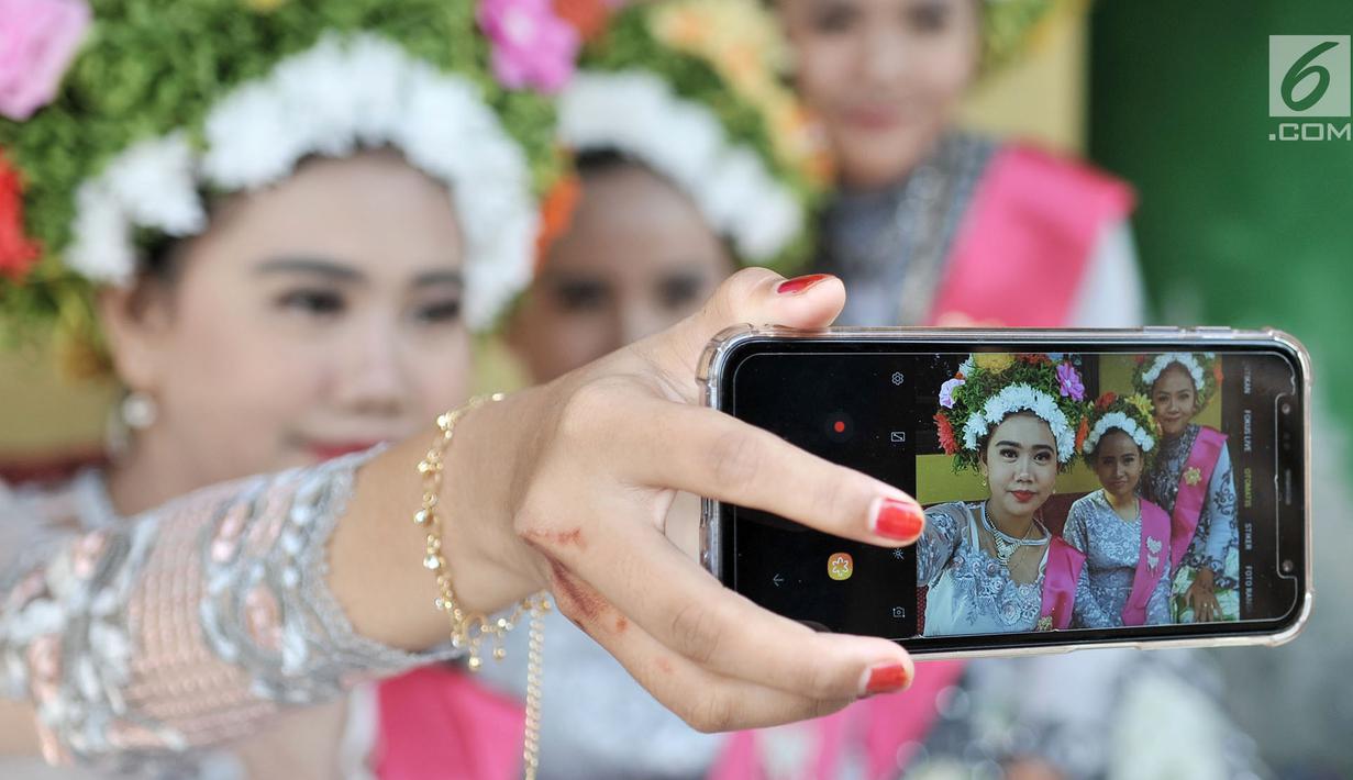 Sejumlah gadis berswafoto saat menunggu upacara adat Ngarot dimulai di Desa Lelea, Indramayu, Jawa Barat, Rabu (19/12). Hari Rabu minggu ketiga di bulan Desember dipercaya oleh masyarakat setempat sebagai hari keramat. (Merdeka.com/Iqbal Nugroho)