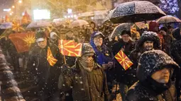 Pengunjuk rasa mengibarkan bendera Macedonia saat menggelar protes di depan gedung Parlemen, Skopje, Selasa (27/2). Di tengah hujan salju, mereka turun ke jalan memprotes wacana pengubahan nama negara mereka. (Robert ATANASOVSKI/AFP)