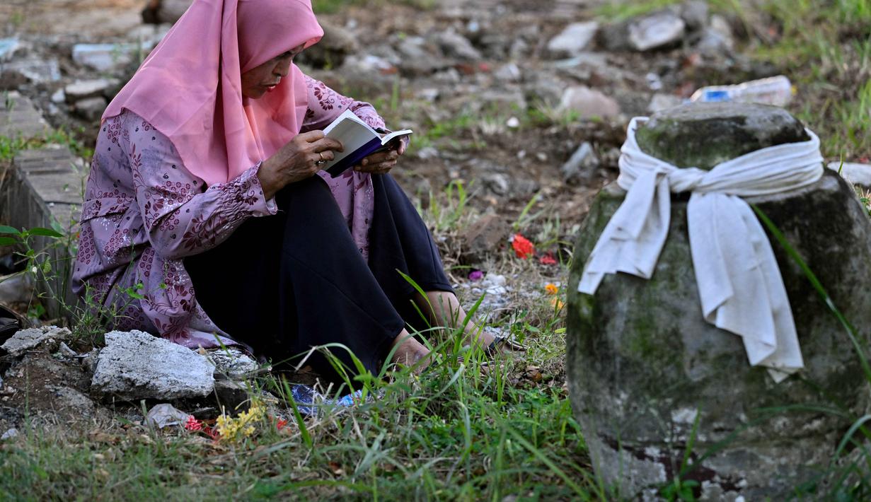 Di akhir November 2025 lalu, sebagian wilayah Aceh, terutama Aceh Tamiang, Bireuen, Pidie, Aceh Utara, Aceh Tengah, dan Nagan Raya, diterjang banjir bandang dan tanah longsor. Tampak dalam foto, seorang wanita membaca Al-Quran sambil berdoa untuk kerabatnya yang meninggal dunia dalam peristiwa gempa dan tsunami Aceh pada 2004 lalu di sebuah kuburan massal di Siron, pada 26 Desember 2025. (CHAIDEER MAHYUDDIN/AFP)