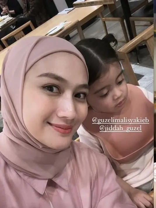 Melody tampil dengan kerudung dan kemeja pink saat hadir di ulang tahun Ameena. [@melodylaksani92]