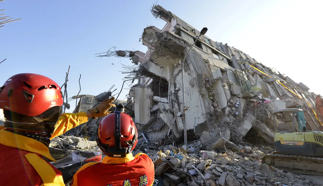 Dua tim SAR berdiri di dekat reruntuhan apartemen yang ambruk akibat gempa di Tainan, Taiwan, Senin (8/2). Dua korban, Tsai Wei-ling dan Lee Tsung-tien, berhasil diselamatkan setelah terperangkap selama lebih dari 50 jam. (AFP PHOTO/Sam Yeh)