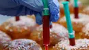 Seorang pekerja meletakkan jarum suntik penuh jeli raspberry di atas berliner (donat Jerman) di toko roti Kreyenbuhl di Muri, Swiss, 5 Februari 2021. Merespons hadirnya vaksin Covid-19, toko roti Kreyenbuhl mencoba merayakannya dengan membuat "Vaccine Berliners". (STEFAN WERMUTH/AFP)