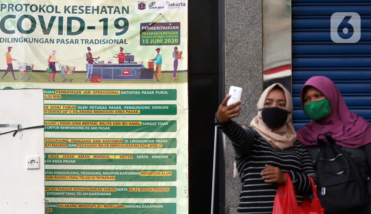Warga berfoto di samping spanduk sosialisasi COVID-19 di Pasar Blok A Tanah Abang, Jakarta, Selasa (1/9/2020). Guna meningkatkan kewaspadaan masyarakat, muspida kecamatan Tanah Abang memajang peti mati dilengkapi data jumlah korban COVID-19 di wilayah tersebut. (Liputan6.comHelmi Fithriansyah)