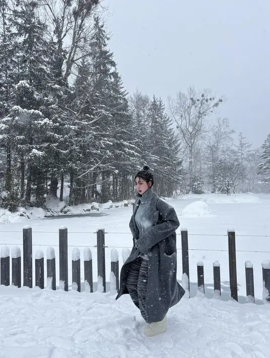 Karina aespa terlihat bermain salju mengenakan outfit monokrom. Karina mengenakan turtleneck abu-abu, ditumpuk long coat, dipadukannya dengan sweat pants yang sama-sama berwarna abu-abu. [Foto: Instagram/katarinabluu]