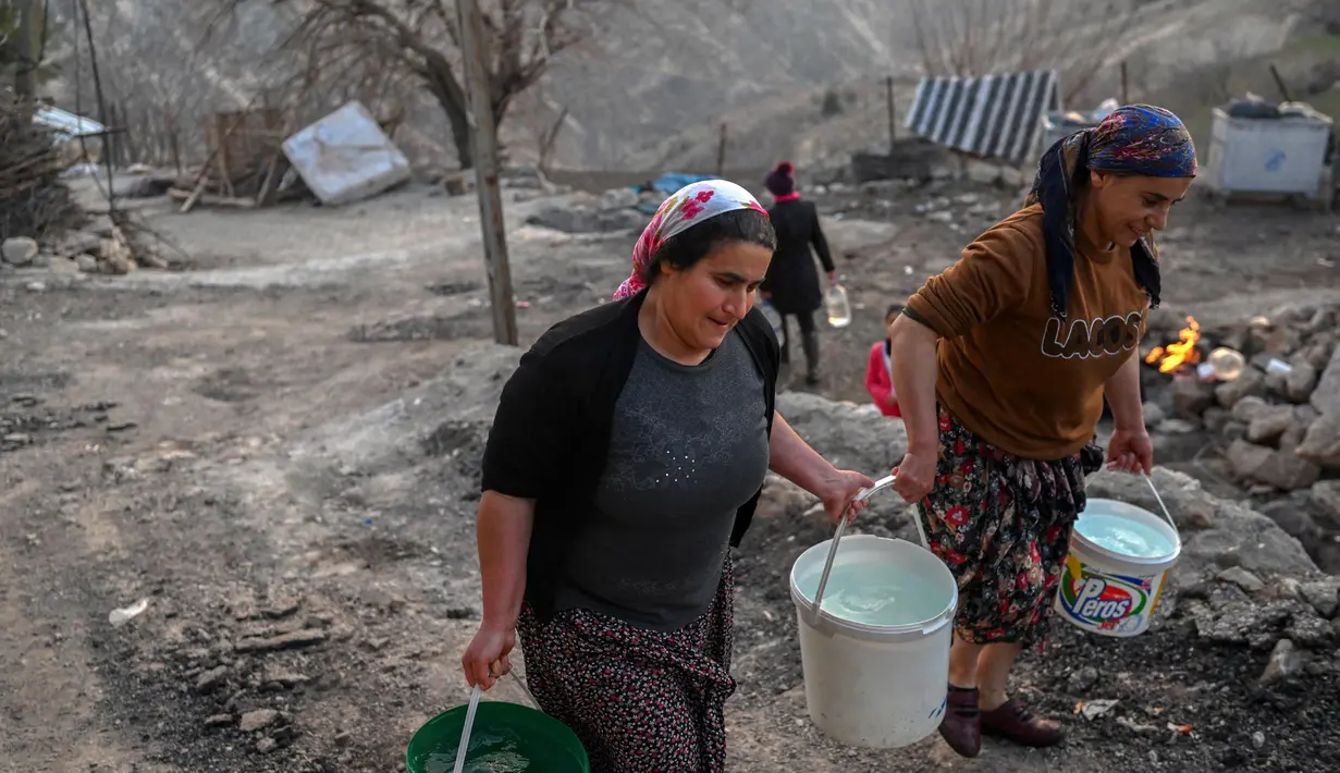 Dua orang wanita membawa ember berisi air di kawasan desa Yaylakonak distrik Adiyaman, Turki, Minggu (19/2/2023). Gempa bumi berkekuatan 7,8 magnitudo melanda dekat Gaziantep, Turki, pada dini hari tanggal 6 Februari, diikuti oleh gempa susulan berkekuatan 7,5 magnitudo setelah tengah hari. Gempa bumi tersebut menyebabkan kehancuran yang meluas di Turki Selatan dan Suriah Utara dan telah menewaskan lebih dari 40.000 orang. (BULENT KILIC/AFP)