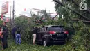 Warga membersihkan dahan pohon tumbang yang menimpa mobil di Kota Tangerang, Banten, Kamis (23/12/2021). Puluhan pohon dan gapura tumbang akibat terjangan angin kencang saat hujan lebat melanda Kota Tangerang. (Liputan6.com/Angga Yuniar)