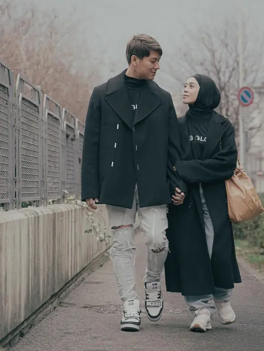 OOTD pasutri Rizky Billar dan Lesti Kejora dengan outfit serba hitam. Rizky Billar tampil mengenakan kaus hitam bercorak tulisan dengan denim abu-abu dan outer coat hitam. Sedangkan Lesti tampil mengenakan kaus yang sama dan celana jeans dan long coat, serta hijab hitam polos. [Foto: Instagram/rizkybillar]