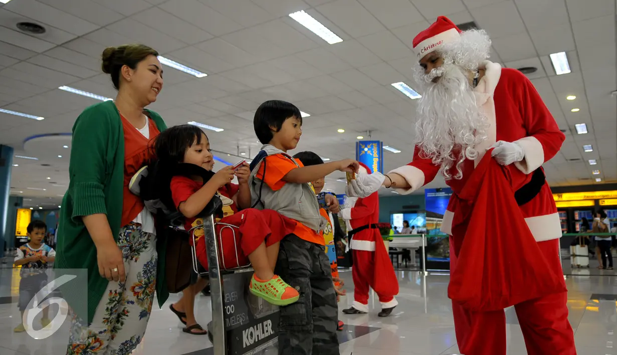 Santa Claus memberikan hadiah kepada anak-anak di Bandara Soekarno Hatta, Tangerang, Banten, Selasa (22/12). Sejumlah orang berkostum santa claus membagikan coklat kepada penumpang yang berada dibandara. (Liputan6.com/Faisal R Syam)