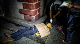 Gambar yang diambil pada 8 Juli 2016 memperlihatkan petugas kepolisian Filipina memeriksa mayat yang diduga seorang pengedar narkoba dengan kondisi kepala terbungkus lakban di sebuah jalan di Manila. (AFP PHOTO/Noel CELIS)