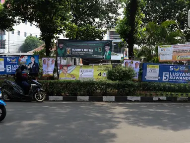 Pengendara motor saat berhenti di samping Alat Peraga Kampanye (APK) yang terpasang di taman kawasan Paseban, Jakarta, Kamis (7/12/2023). (Liputan6.com/Herman Zakharia)