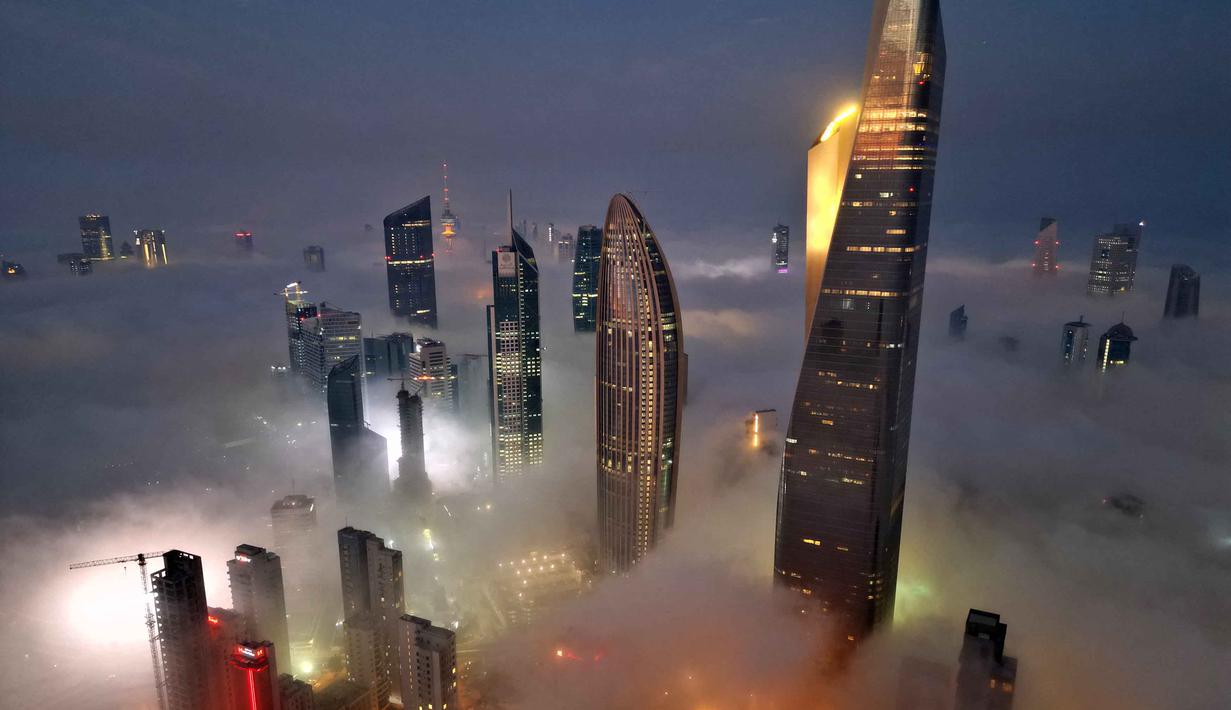 Situasi ini diperkirakan akan menghilang secara bertahap menjelang siang. Tampak foto udara memperlihatkan gedung pencakar langit yang tertutup kabut pagi di Kota Kuwait pada Minggu 9 November 2025. (YASSER AL-ZAYYAT/AFP)