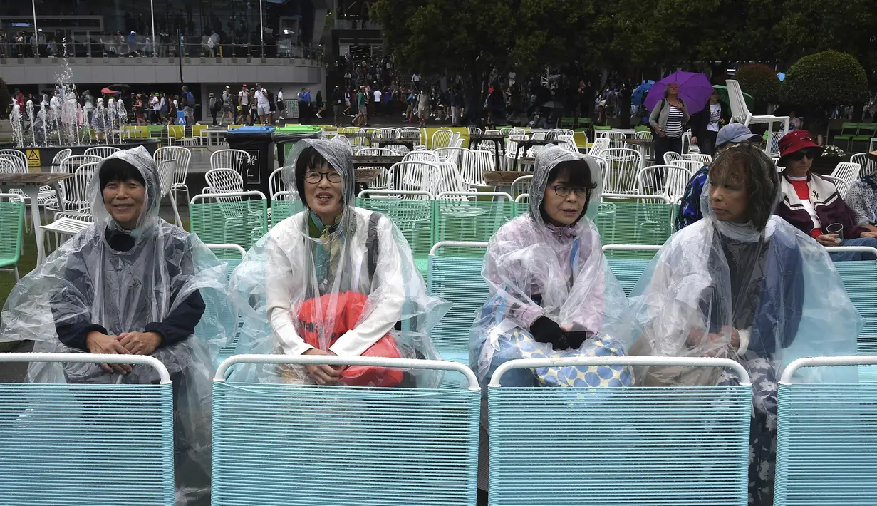 Penonton duduk saat hujan ketika permainan dihentikan di lapangan luar saat pertandingan tunggal putaran pertama mereka di kejuaraan tenis Australia Terbuka di Melbourne, Australia, Senin (20/1/2020). (AP Photo/Andy Brownbill)