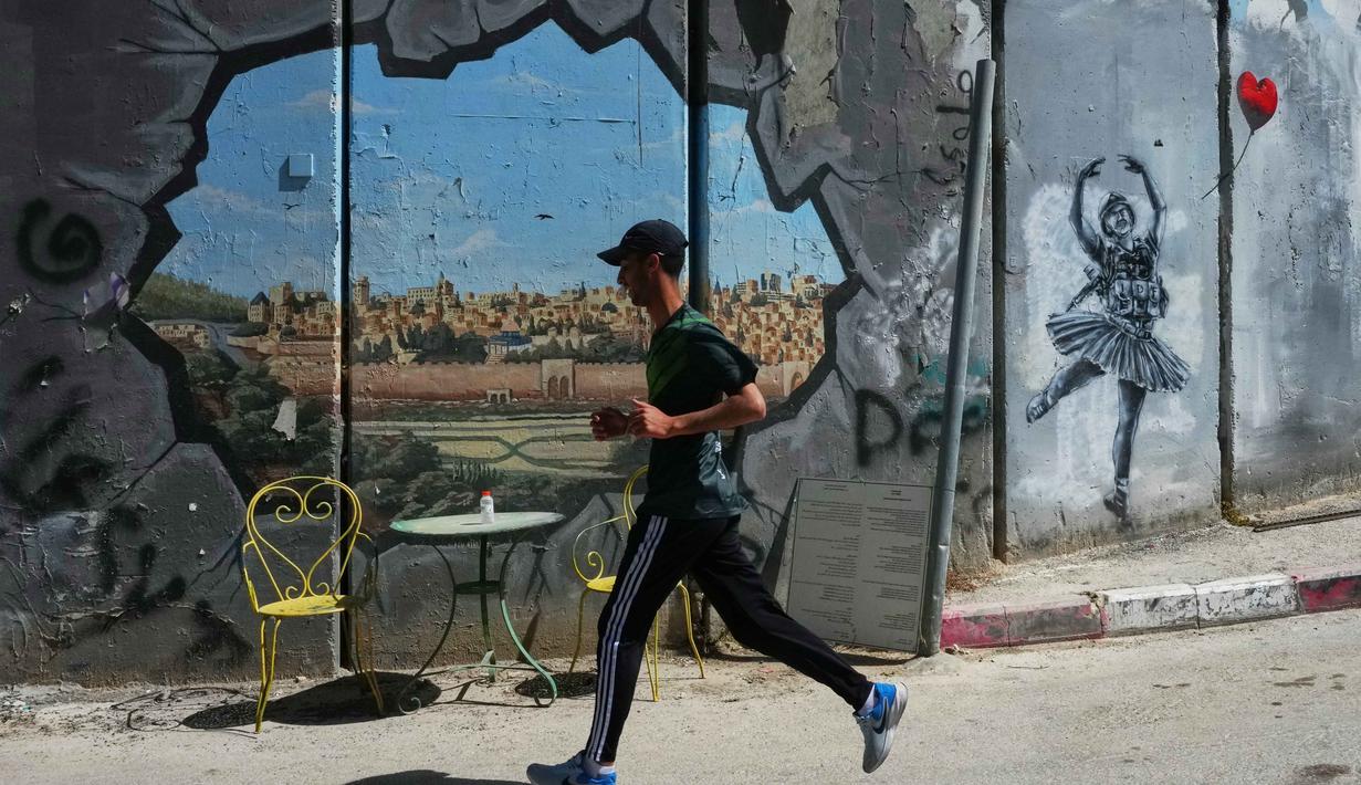 Ajang tahunan ini menekankan solidaritas dan hak untuk bergerak bagi warga Palestina. Tampak dalam foto, seorang pria berlari melewati tembok pemisah Israel saat ia berkompetisi dalam Maraton Palestina di kota Betlehem, Tepi Barat, Jumat 8 Mei 2026. (AP Photo/Mahmoud Illean)