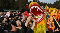 Orang-orang mencoba menyentuh seekor naga saat pertunjukan di sebuah kuil pada hari kedua Tahun Baru Imlek Naga di Beijing pada 11 Februari 2024. (GREG BAKER/AFP)