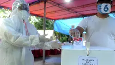 Petugas Kelompok Penyelenggara Pemungutan Suara (KPPS) dengan memakai baju hazmat membantu pemilih memasukkan kertas suara usai menggunakan hak pilihnya dalam Pilkada Tangerang Selatan 2020 di TPS 46, Paku Jaya, Serpong Utara, Rabu (9/12/2020). (merdeka.com/Arie Basuki)