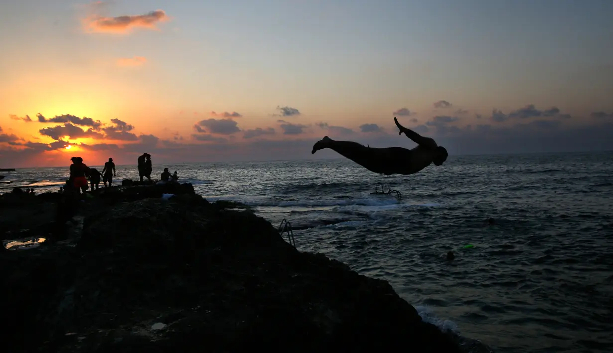 Seorang pria melompat saat berenang di Laut Mediterania dari Corniche, atau promenade tepi laut  saat matahari terbenam pada hari terakhir musim panas, di Beirut, Lebanon (20/9). (AP Photo / Hussein Malla)