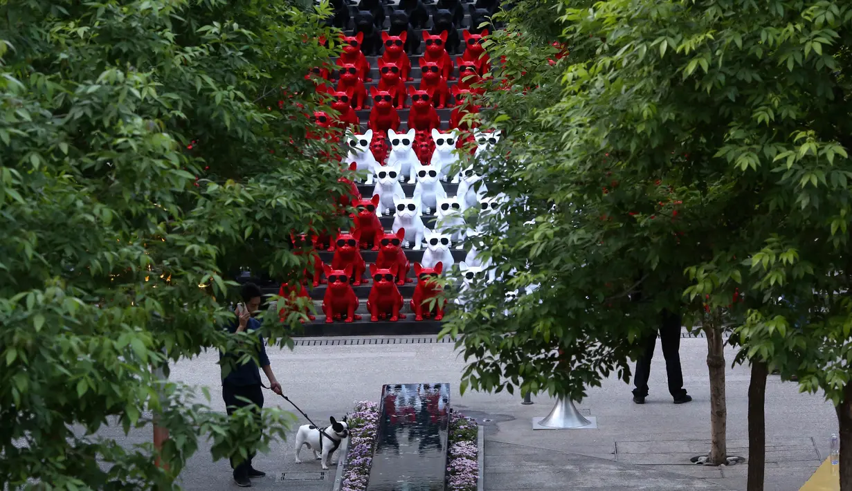 Seorang pria berbicara melalui ponselnya di depan speaker audio yang berbentuk anjing mengenakan kacamata di distrik perbelanjaan di Beijing, China (3/5). (AP Photo / Ng Han Guan)