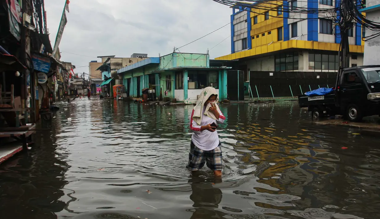 Warga melintasi banjir rob yang terjadi di kawasan Muara Baru, Jakarta Utara, Selasa (14/1/2025). (Liputan6.com/Angga Yuniar)