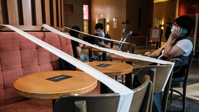 Pelanggan duduk di sebuah kafe, yang memiliki selotip di setiap meja untuk pembatasan jarak sosial, di Hong Kong (21/4/2020). Kepala eksekutif Carrie Lam mengatakan langkah-langkah jarak sosial dan beberapa pembatasan bisnis akan berlanjut selama dua minggu hingga setidaknya 7 Mei. (AFP/Anthony Wall