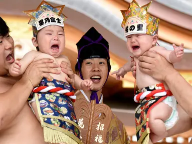 Dua pesumo menggendong bayi yang menangis selama Festival Nakizumo atau kontes bayi menangis di kuil Kamegaike-Hachiman, Jepang, Minggu (14/5). Lebih dari 100 bayi mengikuti kontes menangis yang diyakini bisa membuat bayi sehat. (Toru YAMANAKA/AFP)