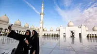 Dua wanita berswafoto dengan latar belakang halaman Masjid Agung Sheikh Zayed di Abu Dhabi, Uni Emirat Arab. Masjid ini menjadi destinasi wisata religi dan landmark yang sering didatangi selebriti, turis dan tokoh dunia. (Photo by Vincenzo PINTO / AFP)
