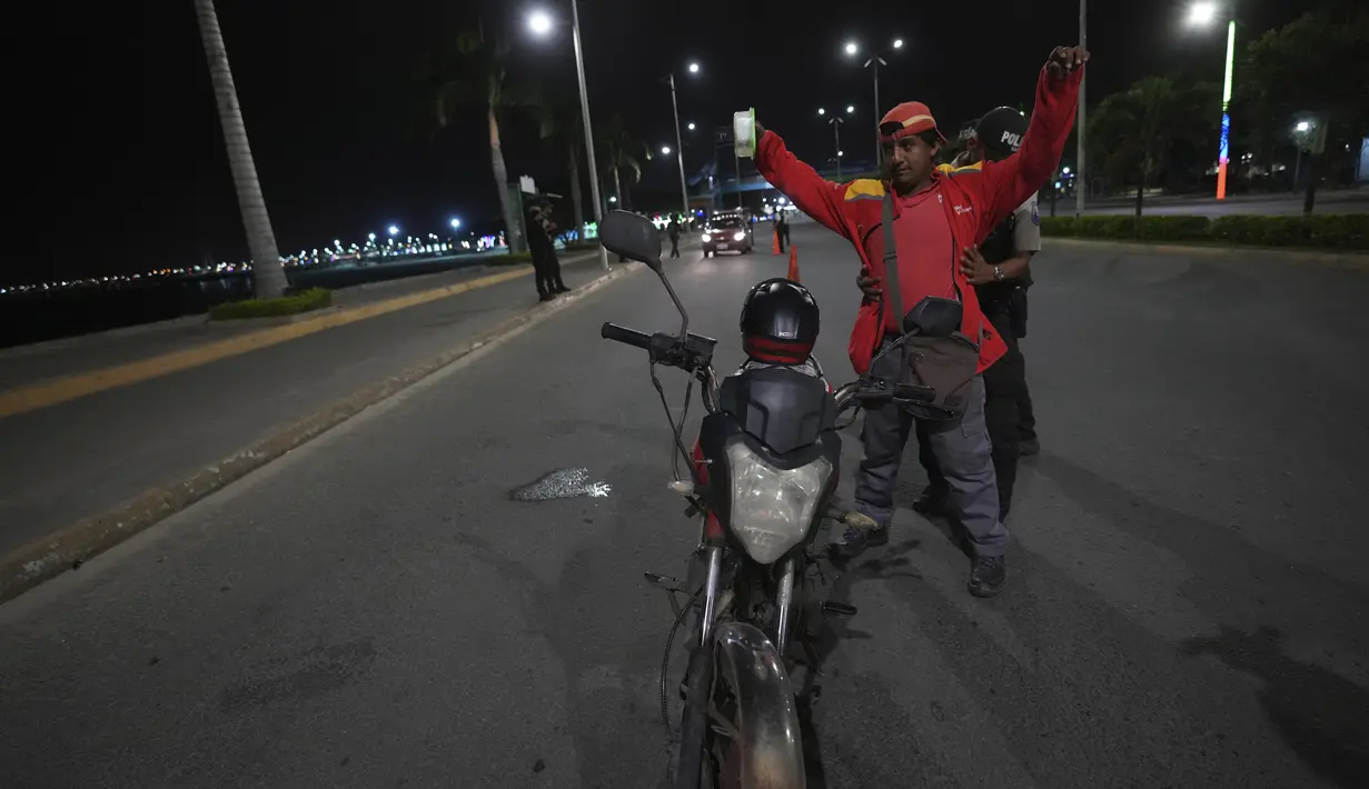 Polisi menggeledah seorang pengendara sepeda motor untuk mencari senjata saat dimulainya jam malam yang ditetapkan oleh Presiden Ekuador Guillermo Lasso guna mengurangi gelombang kekerasan yang sedang berlangsung di Manta, Ekuador, Senin, 24 Juli 2023. (AP Photo/Dolores Ochoa)