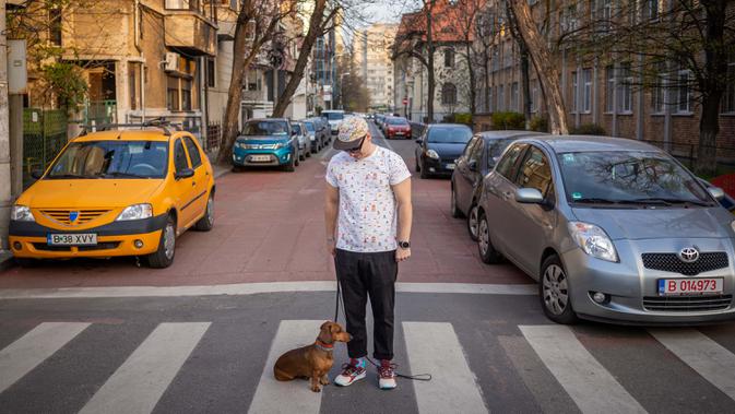 Alexandru Tigoianu (36) berpose dengan anjingnya Tix (3) di Bucharest (29/3/2020). Undang-undang militer, yang disahkan pemerintah Rumania untuk mengurangi penyebaran virus corona, menyatakan berjalan bersama anjing adalah salah satu  kegiatan yang masih diizinkan. (AFP/Andrei Pungovschi)