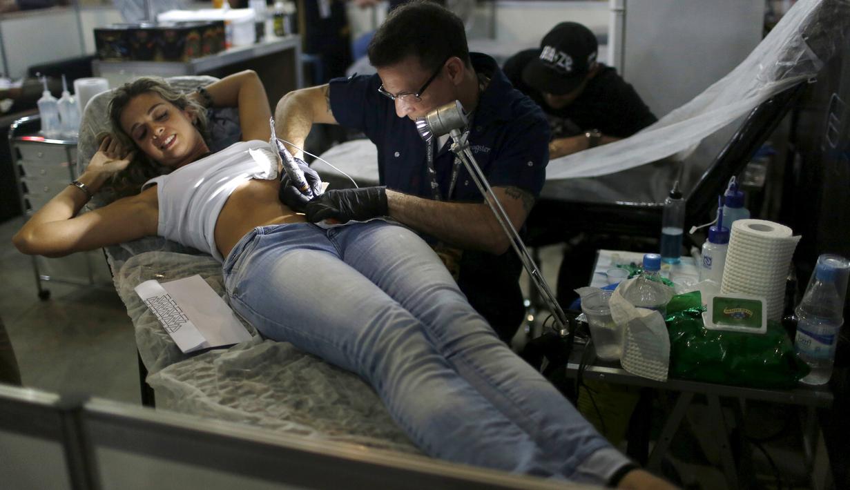 Seorang seniman saat menato seorang perempuan dibagian perutnya saat Festival Internasional Tattoo Week Rio 2016 ketiga di Rio de Janeiro, Brasil, (22/1/2016). (REUTERS/Pilar Olivares)