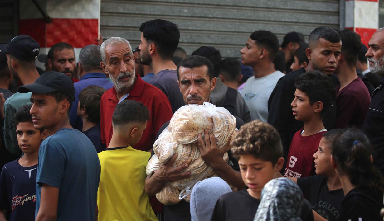 Seorang pria Palestina membawa kantong-kantong roti setelah menerima bantuan dari toko roti amal di kamp pengungsi Nuseirat, yang terletak di Jalur Gaza tengah, pada 2 November 2025. Bantuan tersebut mencakup makanan, obat-obatan, suplemen gizi, serta bahan untuk tempat tinggal. (EYAD BABA/AFP)