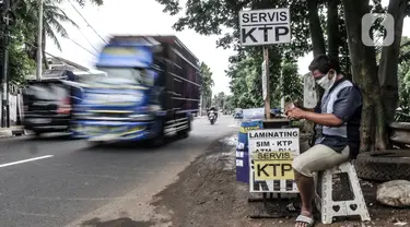 Feri (28) saat menyelesaikan jasa servis kartu tanda penduduk (KTP) di Jakarta, Kamis (21/1/2021). Bermodal meja lipat, poster, dan peralatan pendukung seperti lem, korek api, serta plastik laminating, Feri membuka jasa servis kartu identitas di pinggir jalan Ibu Kota. (merdeka.com/Iqbal S. Nugroho)