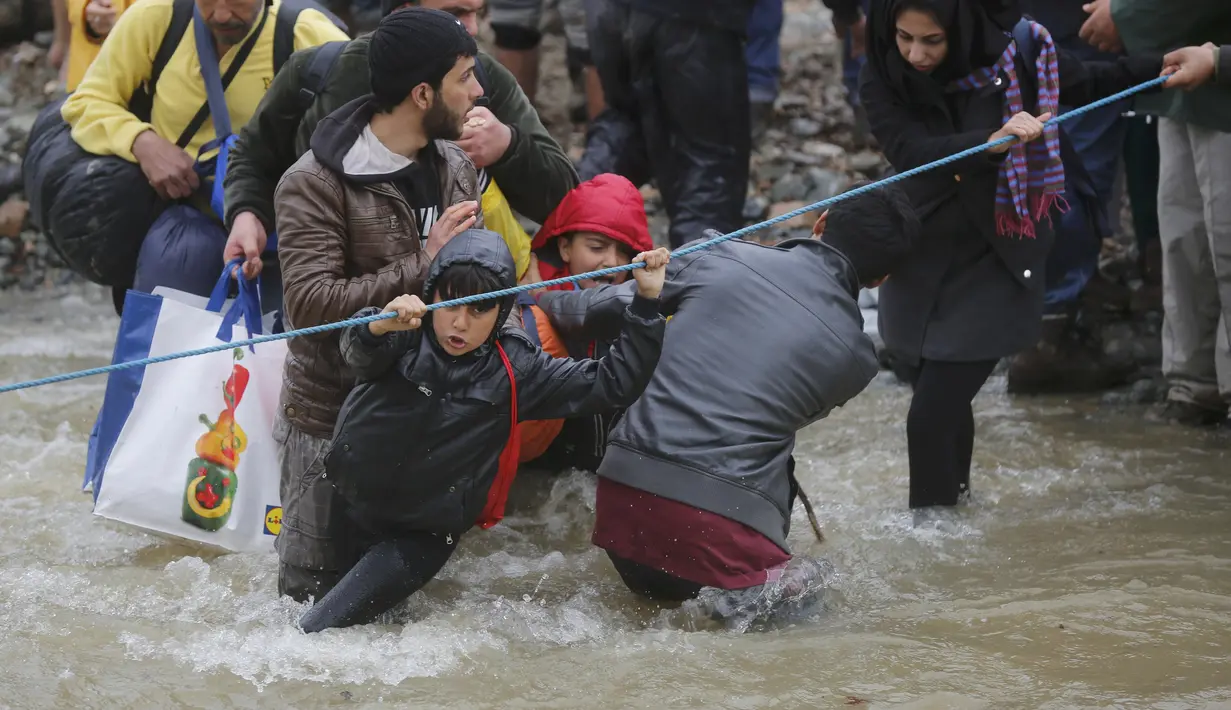 Ribuan migran menyeberangi sungai dengan berpegangan pada seutas tali di perbatasan Yunani-Makedonia, Idomeni, Yunani (14/3/2016). Lebih dari 1.000 migran nekat menembus sungai untuk mencari jalan keluar perbatasan. (Reuters/Stoyan Nenov)