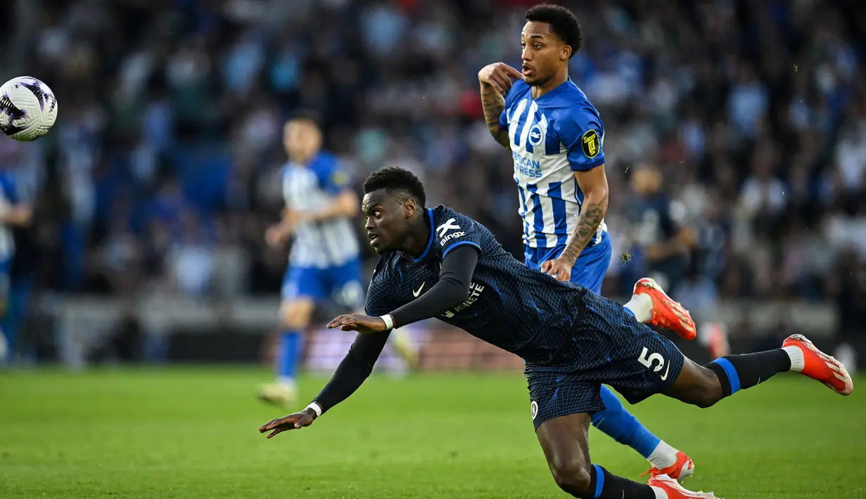 Bek Chelsea, Benoit Badiashile (kiri) terjatuh saat perebutan bola dengan striker Brighton and Hove Albion, Joao Pedro pada laga tunda pekan ke-34 Liga Inggris 2023/2024 di American Express Community Stadium, Brighton, Rabu(15/5/2024). (AFP/Glyn Kirk)