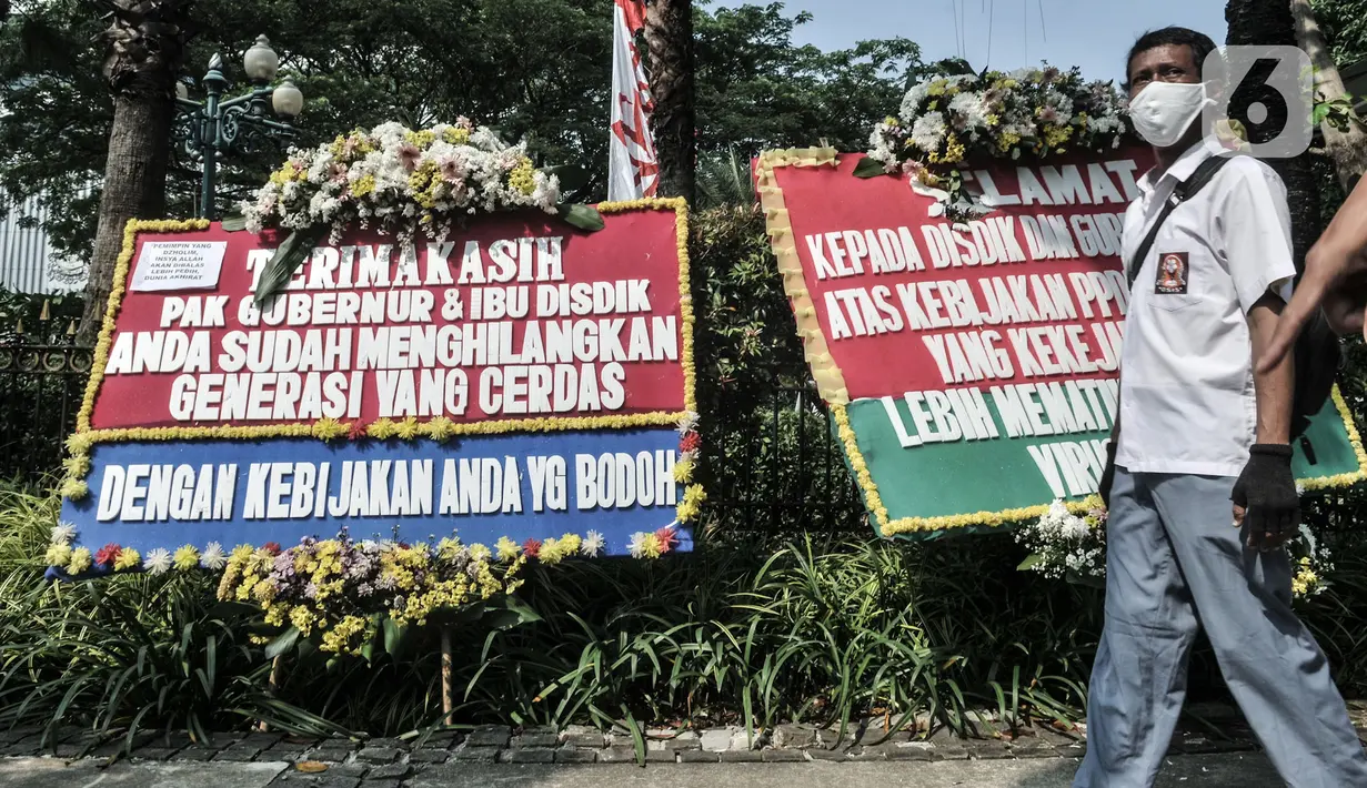 Massa dari Relawan PPDB DKI Jakarta 2020 melintas di depan karangan bunga yang terpajang di Balai Kota DKI Jakarta, Senin (6/7/2020). Karangan bunga itu bentuk kekecewaan terhadap Gubernur Anies Baswedan dan Kadisdik DKI terkait penerimaan siswa baru Jalur Zonasi. (merdeka.com/Iqbal Nugroho)