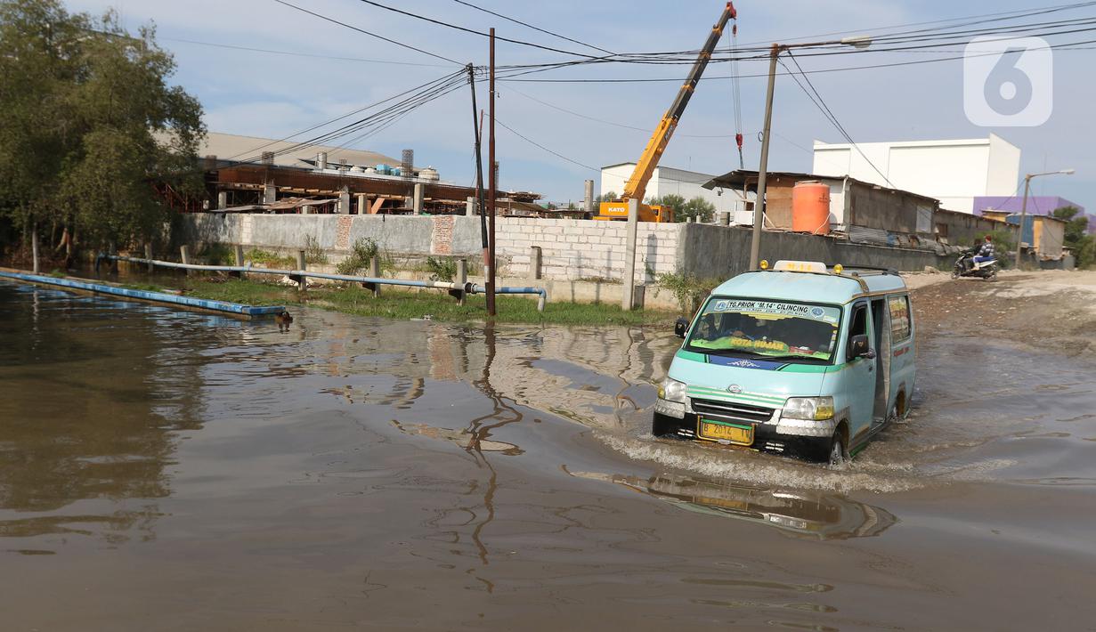 Sebuah angkutan umum (angkot)  melintasi banjir rob di kawasan Pelabuhan Perikanan Samudera Nizam Zachman, Muara Baru, Jakarta, Sabtu (6/11/2021). Banjir rob tersebut disebabkan karena naiknya permukaan air laut. (Liputan6.com/Herman Zakharia)